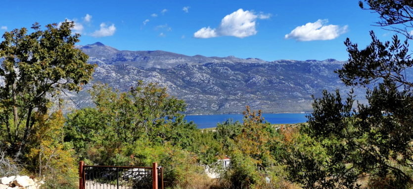 Blick vom Grundstück auf Velebitgebirge und Meer des Velebitkanals mit Bäumen und klarem blauen Himmel in blühender malerischer Landschaft.
